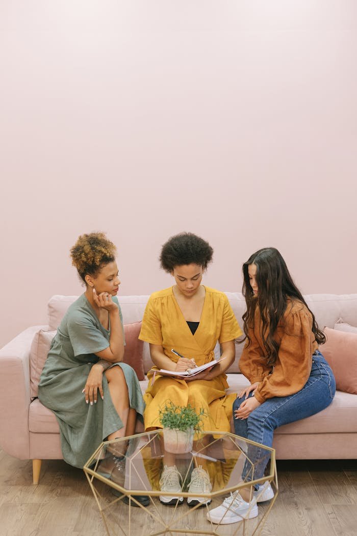 Three women sitting on a couch in a casual office setting, working together on a project.